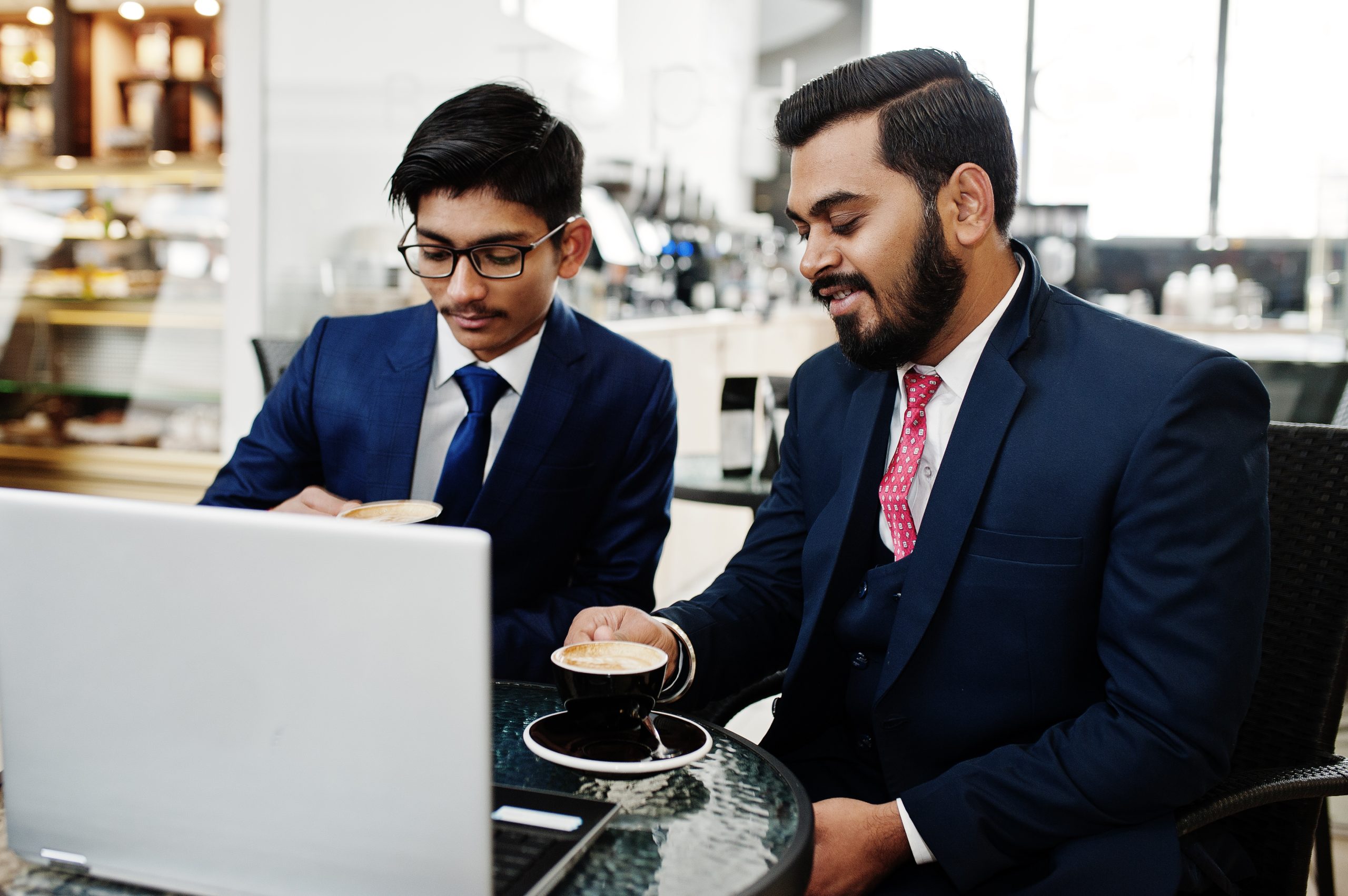 two indian business man in suits sitting at office on cafe, look